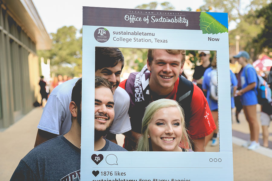 Students pose with an Office of Sustainability poster frame.