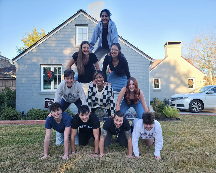 A group of young people forming a human pyramid in front of a house decorated for the holidays.